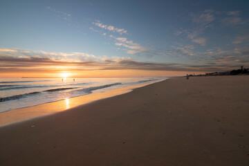 A beautiful sunset on the beach of Mazagon, Spain. In the background the silhouettes of two surfers.