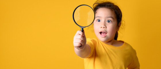 Portrait of surprised cute  little asian girl looking through a magnifying glass. Education concept.