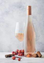 Glass and bottle of pink rose wine with grapes and corkscrew on light background.