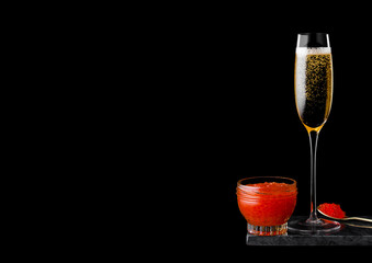 Elegant glass of yellow champagne with red caviar on golden spoon and glass container of caviar on...