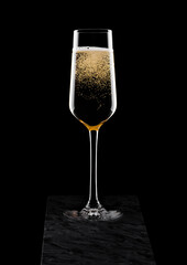 Elegant glass of yellow champagne with bubbles on black marble board on black background.