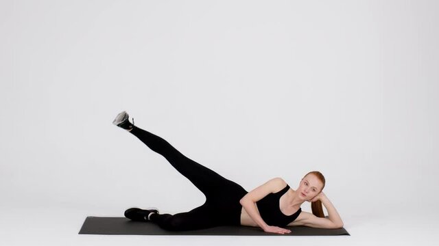 Young Sporty Woman Doing Side Leg Lift Exercise In Studio