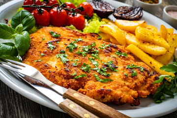 Breaded fried pork chop with French fries and vegetables on wooden table
