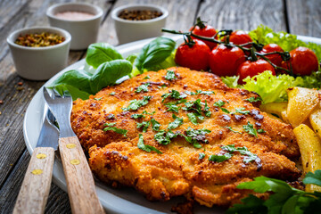 Breaded fried pork chop with French fries and vegetables on wooden table
