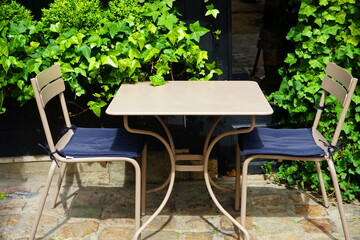 Light metal outdoor chairs and  table in city street cafe. Ivy landscaping with garden furniture. Side view of terrace seating area in the garden.