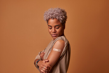 Vaccinated embarrassed African American woman demonstrates hand with plaster at vaccination site...
