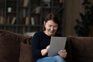 Elderly people and modern tech. Aged female pensioner sit on sofa hold touchpad surf internet order...