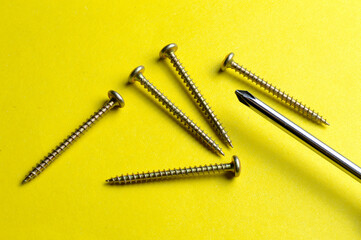 several screws and a screwdriver lie on a yellow background. close-up.