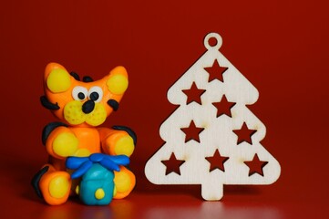 Toy tiger made of plasticine with Christmas toys on a red background.