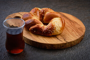 Turkish tea in traditional glass and traditional turkish pastry acma. Baked sesame encrusted bagel lies on wooden board at dark background. Traditional turkish breakfast meal