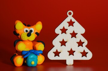 Toy tiger made of plasticine with Christmas toys on a red background.
