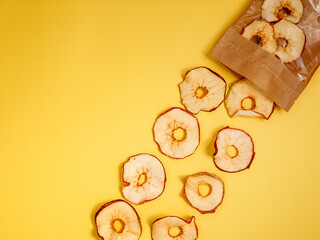 Organic homemade dehydrated Apple fruit chips on yellow background spilled out of eco paper...