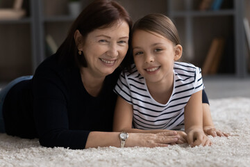 Emotional bonding. Portrait of senior female grandma aged foster mom lying on carpet embracing...