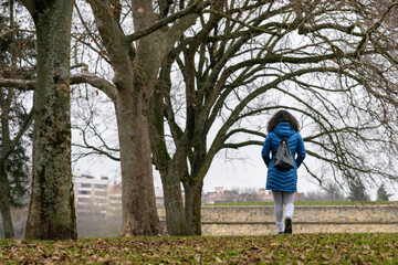 Woman in the park in winter under the trees with blue coat