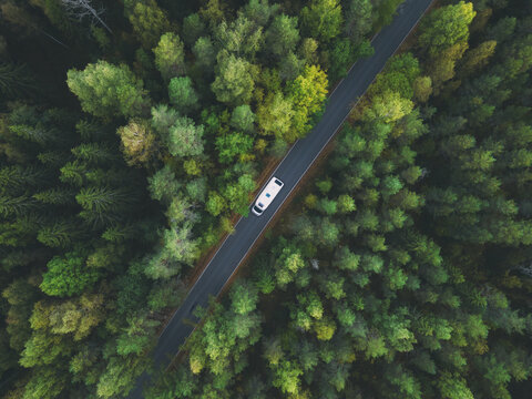 White camper van with solar panels drive through green forest. Aerial top down view. Travel concept.