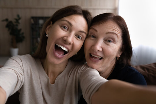 Kidding with mommy. Joyful grown daughter joking laughing taking funny selfie together with retired mother. Young and elderly women two sisters mom and adult child have fun at home shoot self portrait
