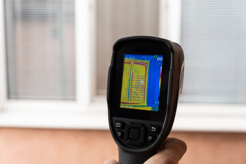 A male hand holds a thermal imager at the window of a house. Search for heat loss in private houses.