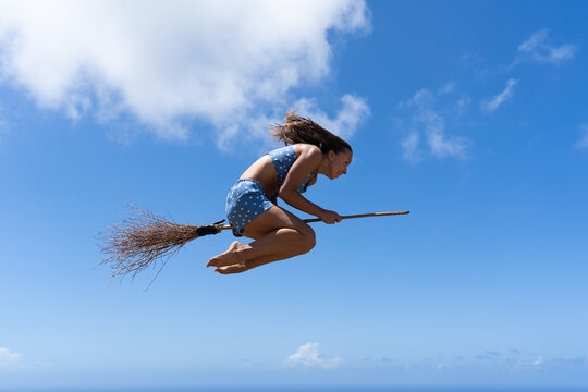 Young woman on the broom pretending to be witch on sky background