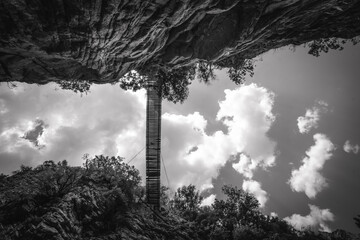 Black and white photo of hiking foot bridge and clouds at top of cliff