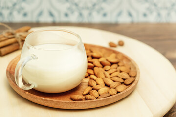 Non diary milk. Vegan food composition with cup of almond milk and almond nuts on a wooden plate and cinnamon sticks on a eco friendly kitchen. Rustic still life with vegan healthy product