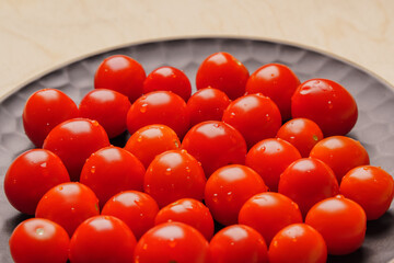 Red cherry tomatoes covered with drops of water lie on a dark plate