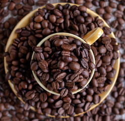 A cup filled with coffee beans surrounded by coffee beans. Cutting board, recipe, advertisement, catalog, menu, website, poster, postcard. Coffee beans close up. Dried and roasted coffee beans.