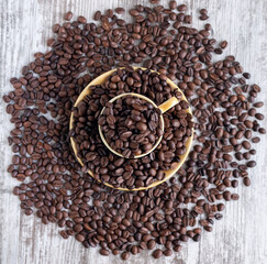 A cup filled with coffee beans surrounded by coffee beans. Cutting board, recipe, advertisement, catalog, menu, website, poster, postcard. Coffee beans close up. Dried and roasted coffee beans.