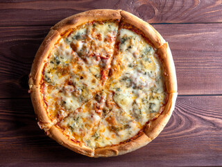 Close-up of a ready-made Italian pizza with four cheeses on a brown wooden background. Top view, flat lay. A traditional dish of Italian cuisine. Home cooking