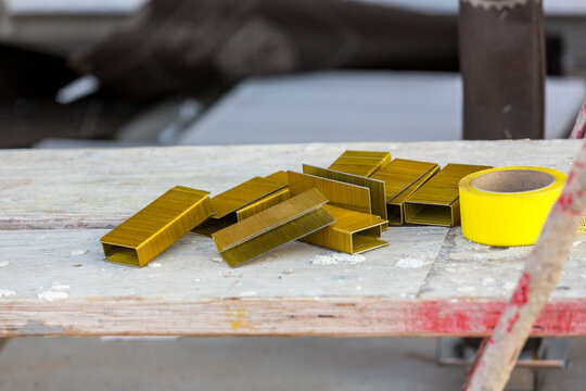 Pile of large construction staples heaped together on a scaffolding surface with yellow tape