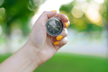 Hand with compass on green blurred background with sun glare at sunset sky