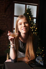 Happy blonde woman with vintage glass of champagne on dark background with christmas tree lights