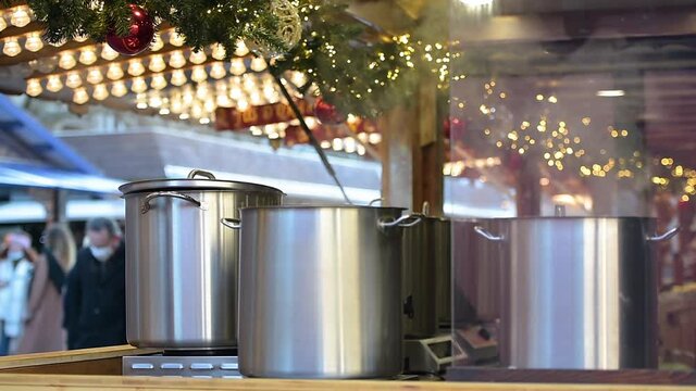 Multiple stainless steel bowl with steaming mulled wine hot wine inside food market stall chalet at annual Christmas market in strasbourg, France - silhouette of people customers tourists in backgroun