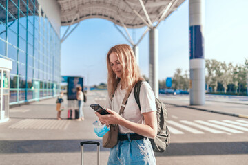Tourist traveler girl with backpack and suitcase uses a mobile smartphone near the international airport