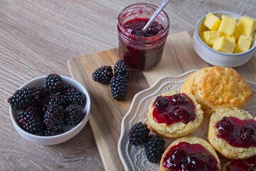 Scones on a decorative plate with homemade blackberry jam. Glass jar with jam and fresh blackberries on a wooden board