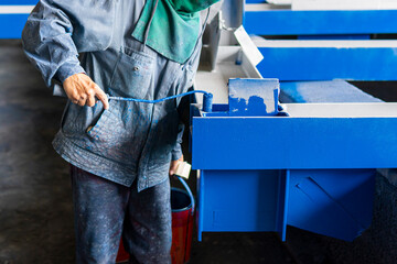 Painter is using a paint roller for painting blue color on a steel structure piece at industrial factory.