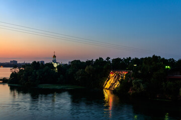Night view of Monastyrsky Island with illuminated artificial waterfall "Roaring Threshold" and a small church of Saint Nicholas in Dnipro, Ukraine
