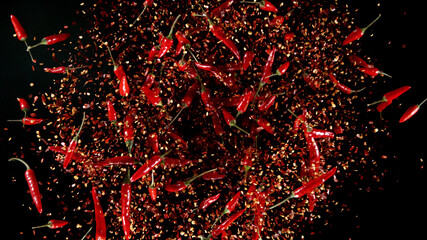 Freeze motion of flying chilli peppers on black background.