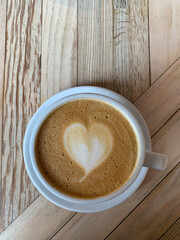 Selective focus of cup of coffee latte. A mug of flat white coffee on a wooden background. Coffee art. Heart shape latte art. Vertical 