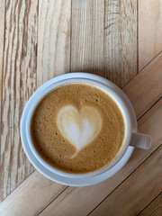 Selective focus of cup of coffee latte. A mug of flat white coffee on a wooden background. Coffee art. Heart shape latte art. Vertical 