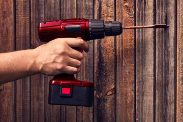 A drill in his hand drills a wooden door .Handmade work. The tool is in the hands of a man.