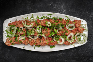 LULYA-KEBAB with herbs and onions on a plate, on a dark background