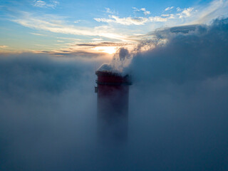 High chimney of a thermal power plant above the fog in the rays of the sunset. Aerial drone view.