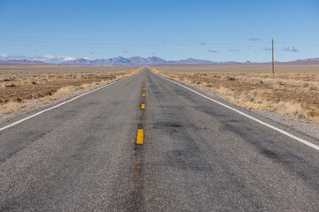 Lonely asphalt road stretches into the middle of nowhere in the desert lined by power poles
