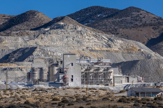 Industrial buildings for mining operation sits in front of large tailing piles in front of a mountain