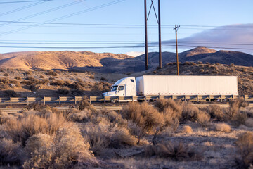 White anonymous semi truck drives down remote desert highway beneath power lines