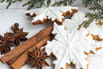 Gingerbread cookies in white glaze, cinnamon, spices and juniper branches on a light wooden background. Christmas gingerbread. Edible Christmas decor concept. Christmas traditions. Copy space. Flat la - 475905456