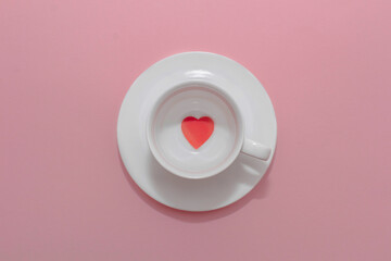 White cup with a saucer and a heart inside on a pink background. Valentines day concept