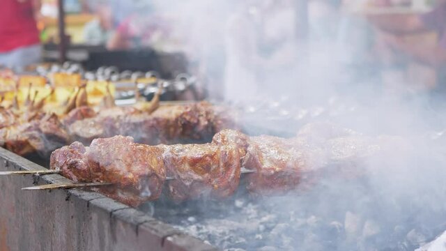 Grilling Juicy Shish kebab outdoors. Barbecue, grilled meat on a charcoal grill in smoke. Chef rotates the fried pork on a skewer. Street Food trade. Lots of hungry people tourist on festival. 4K.