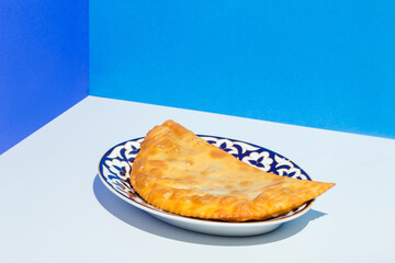 Homemade chebureks with stuffing and herbs in traditional Caucasian plate on blue