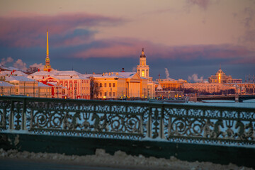 Winter panoramic view of St. Petersburg at sunset, golden spire of Peter and Paul fortress, Kunstkamera tower, embankment with bridge on background, steam over frozen Neva river, sky of orange color